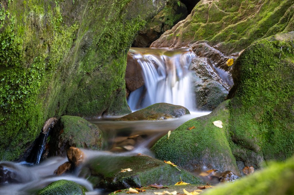 Kleine Waldkaskade zwischen moosbewachsenen Felsen im Müllerthal in Luxemburg