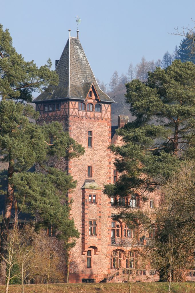 Schloss Saareck in Mettlach mit rotem Turm zwischen hohen Bäumen